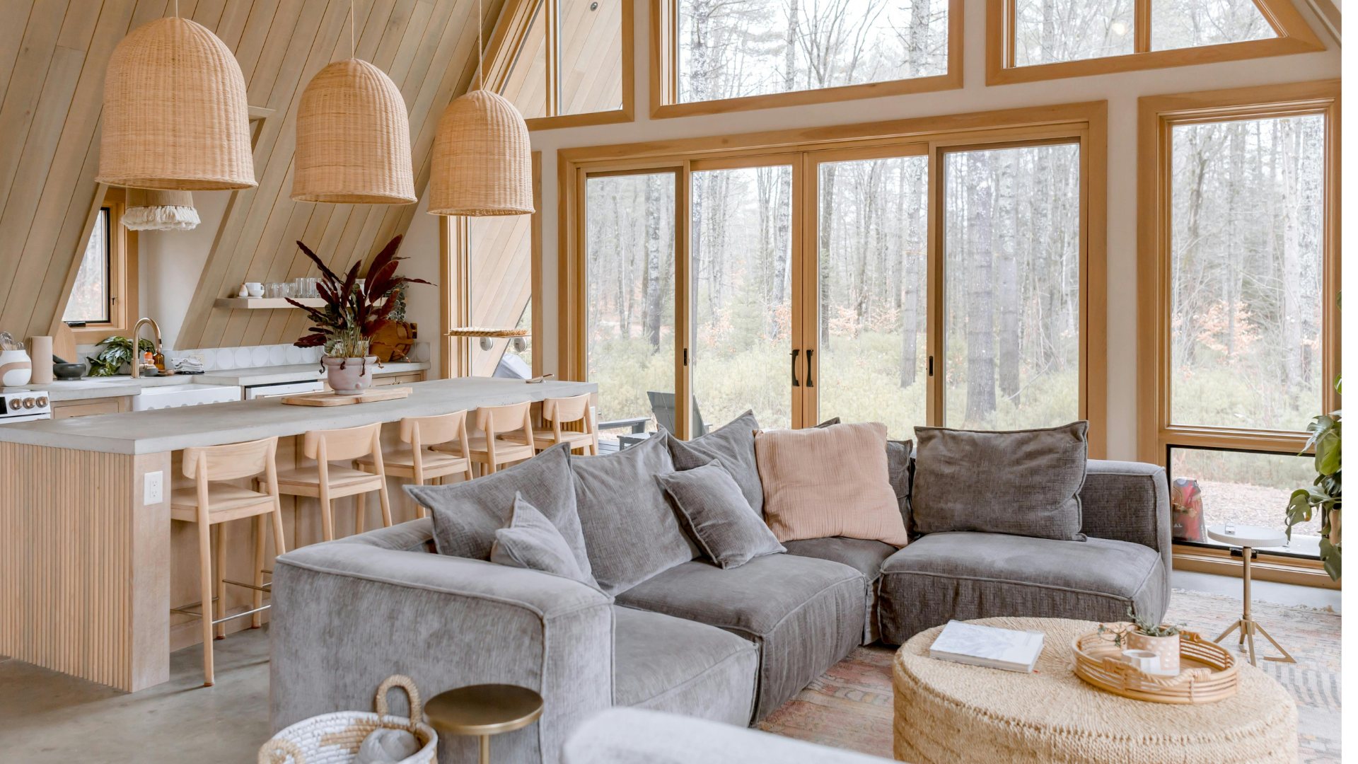 A bright timber-framed cabin interior with a kitchen island and forest views